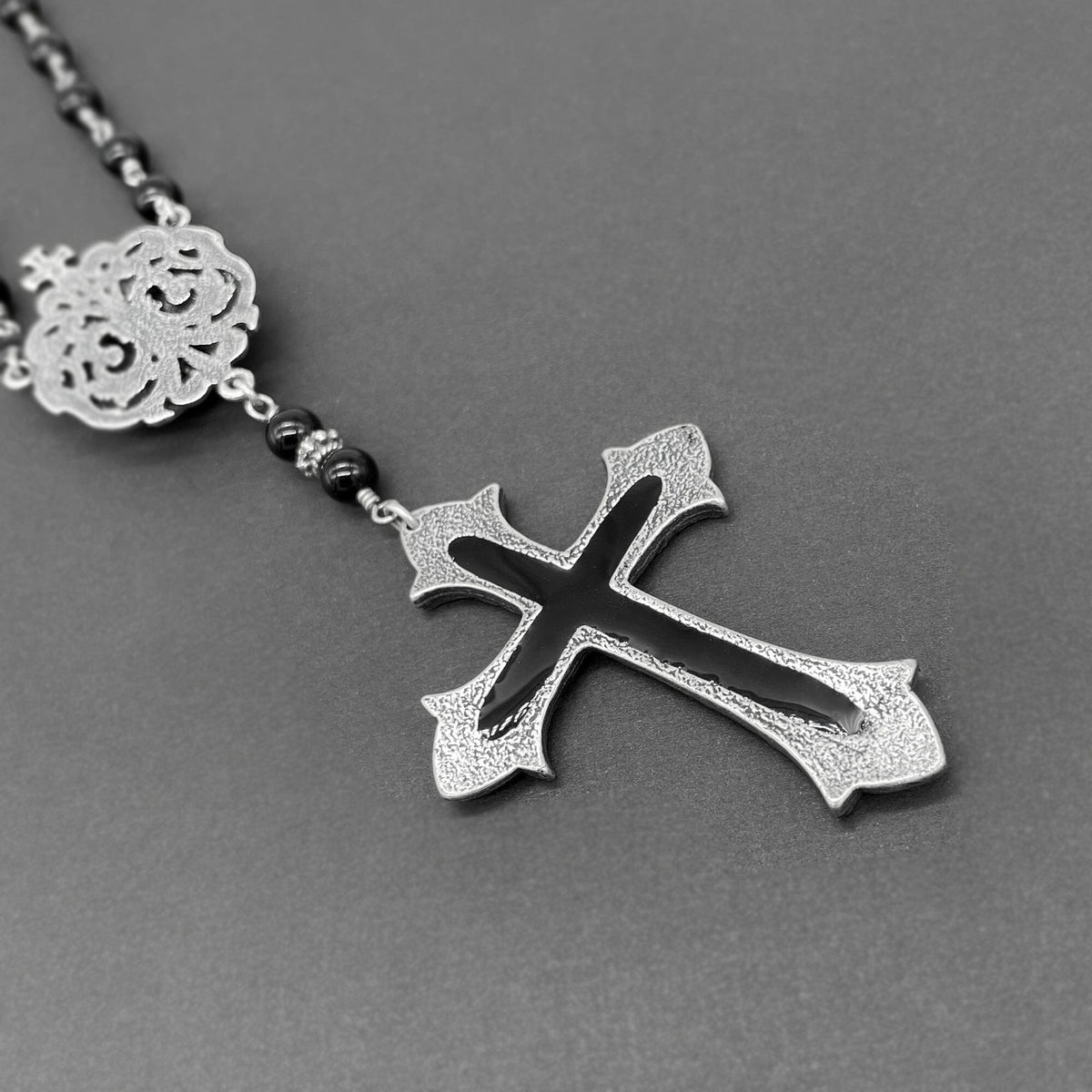 Close up view of the back of the silver cross on the black beaded rosary necklace